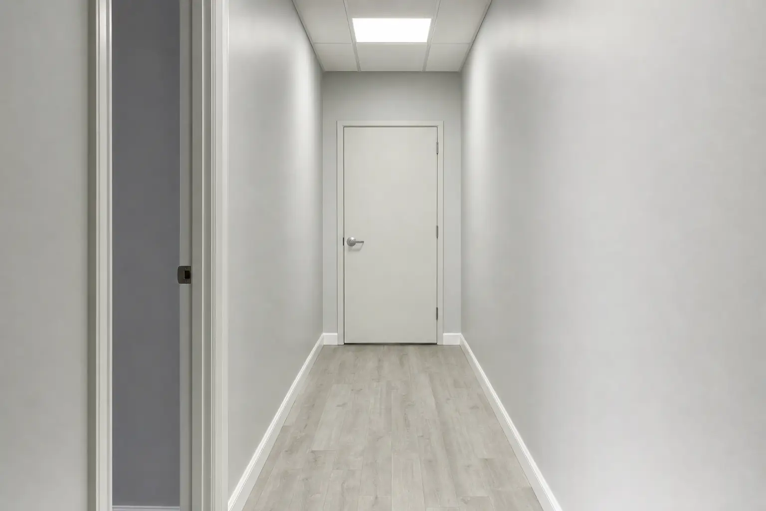 Couloir de rez-de-chaussée sous un plafonnier diffus, aucune fenêtre, aucune décoration.